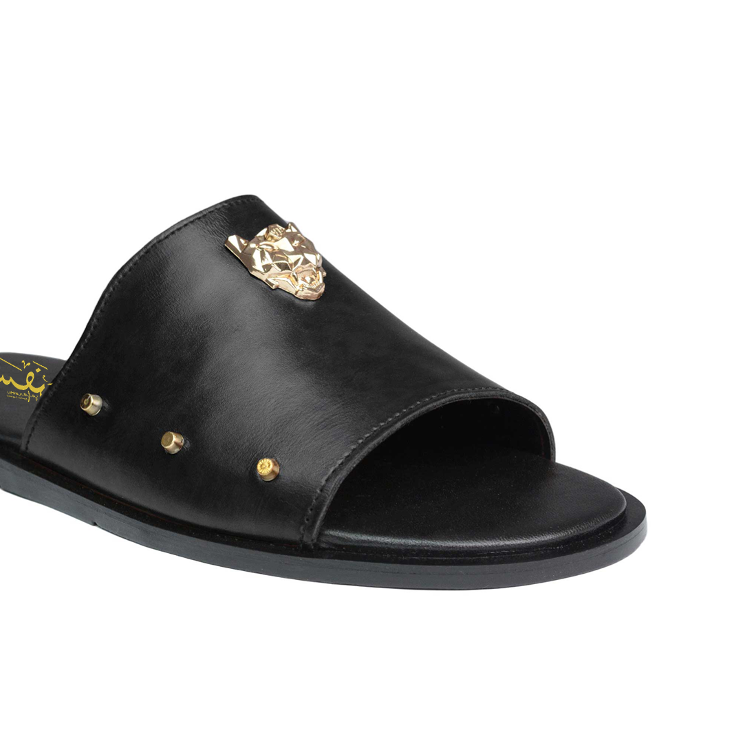 Black sandal with gold embellishments on a white background